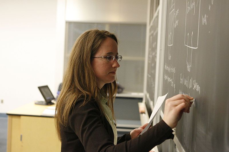 a techer writes on a classroom chalkboard