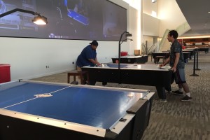 Two men stand at a table playing air hockey before the tournament begins.