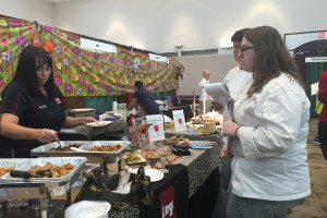 Student Brooke Simmons waits in line at a booth as a vendor scoops teriyaki chicken onto a plate for her to taste.