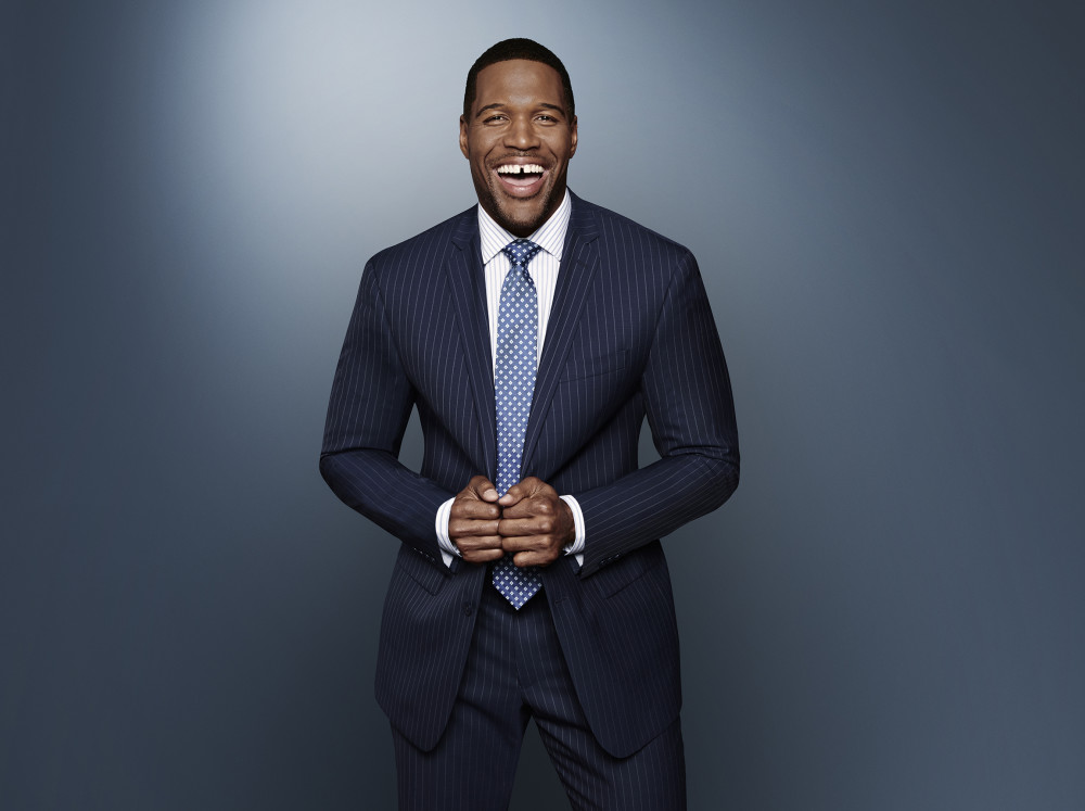 Michael Strahan smiling in navy suit.