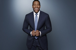 Michael Strahan smiling in navy suit.