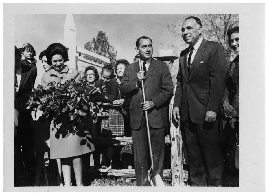 Photograph of Lady Bird Johnson and Henry B. Gonzalez standing by a fence with other people.