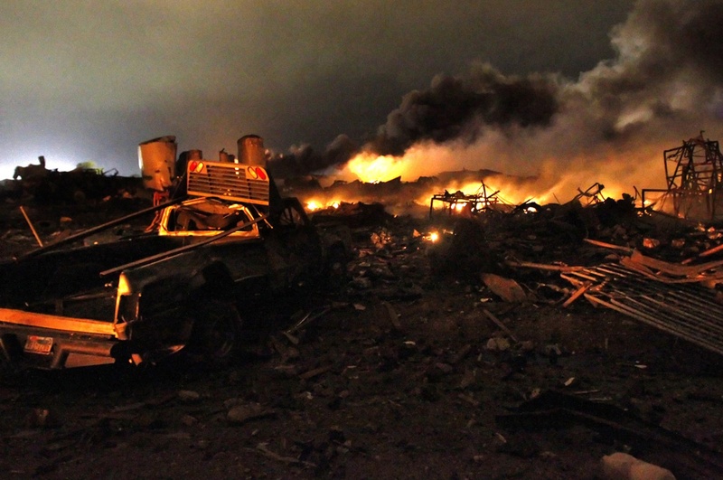 A vehicle near the remains of a fertilizer plant burning after an explosion