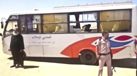 This image released by the Minya governorate media office shows a policeman and a priest next to a bus after stormed the bus in Minya, Egypt, Friday, May 26, 2017. Egyptian officials say dozens of people were killed and wounded in an attack by masked militants on a bus carrying Coptic Christians, including children, south of Cairo. (Minya Governorate Media office via AP)