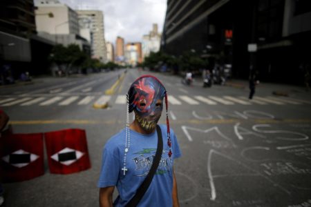 A demonstrator wearing a mask adorned with rosaries stands near a barricade during a 48-hour general strike beginning Wednesday in protest of government plans to rewrite the constitution in Caracas, Venezuela, Wednesday, July 26, 2017. President Nicolas Maduro is promoting the constitution rewrite as a means of resolving Venezuela's political standoff and economic crisis, but opposition leaders are boycotting it. (AP Photo/Ariana Cubillos)