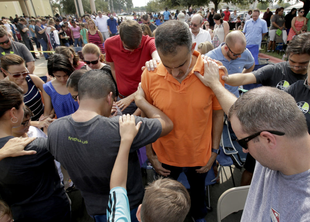 Church members gather to pray around flood victim Carlos Ochoa during Sunday service in the parking lot of the First Baptist Church Sunday, Sept. 3, 2017, in Humble, Texas. The church building was flooded with two feet of water from Hurricane Harvey prompting services to be held in the parking lot for about 2,000 people. 