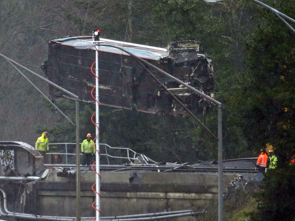 A damaged Amtrak train car is lowered from an overpass Tuesday at the scene of a train crash onto Interstate 5 a day earlier in DuPont, Wash. Federal investigators say they don't yet know why the Amtrak train was traveling 50 mph over the speed limit when it derailed. The rail cars will be taken to a nearby military base for closer analysis.