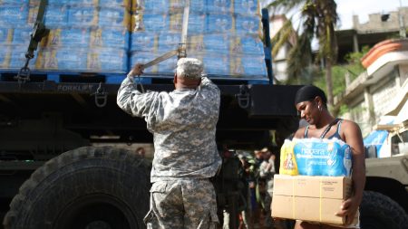 A U.S. Army soldier unloads a shipment of water provided by FEMA as a resident walks past in San Isidro, Puerto Rico