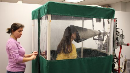Undergraduate Shira Rubin gamely demonstrates the Gesundheit machine, which collects samples of virus from the breath that sick students exhale. Rubin helps Dr. Somayeh Youssefi (left) set up the machine before patients use it.