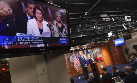 House Minority Leader Nancy Pelosi of Calif., is shown on television as she speaks from the House floor on Capitol Hill in Washington, Wednesday, Feb. 7, 2018, as a news conference that she was supposed to attend goes on in the background.