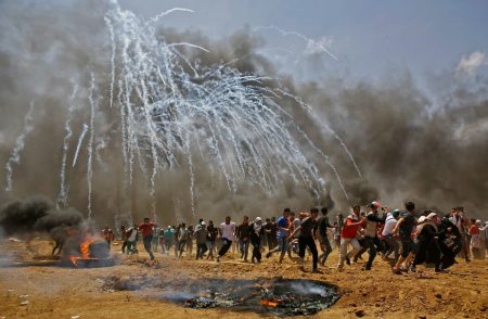Palestinians run for cover from tear gas during clashes with Israeli security forces near the border between Israel and the Gaza Strip.