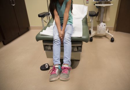 A young girl waits for care in a medical clinic. A growing number of citizen children of immigrant parents are losing out on Medicaid because their parents fear deportation.