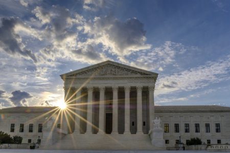 The sun flares in the camera lens as it rises behind the U.S. Supreme Court building in Washington.