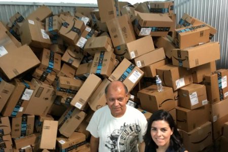 In this photograph taken June 24, 2018, Catholic Charities of the Rio Grande Valley staffer Eli Fernandez and volunteer Natalie Montelongo pose for a photo as they stand by a pile of unsorted Amazon boxes packed with donations in McAllen, Texas.