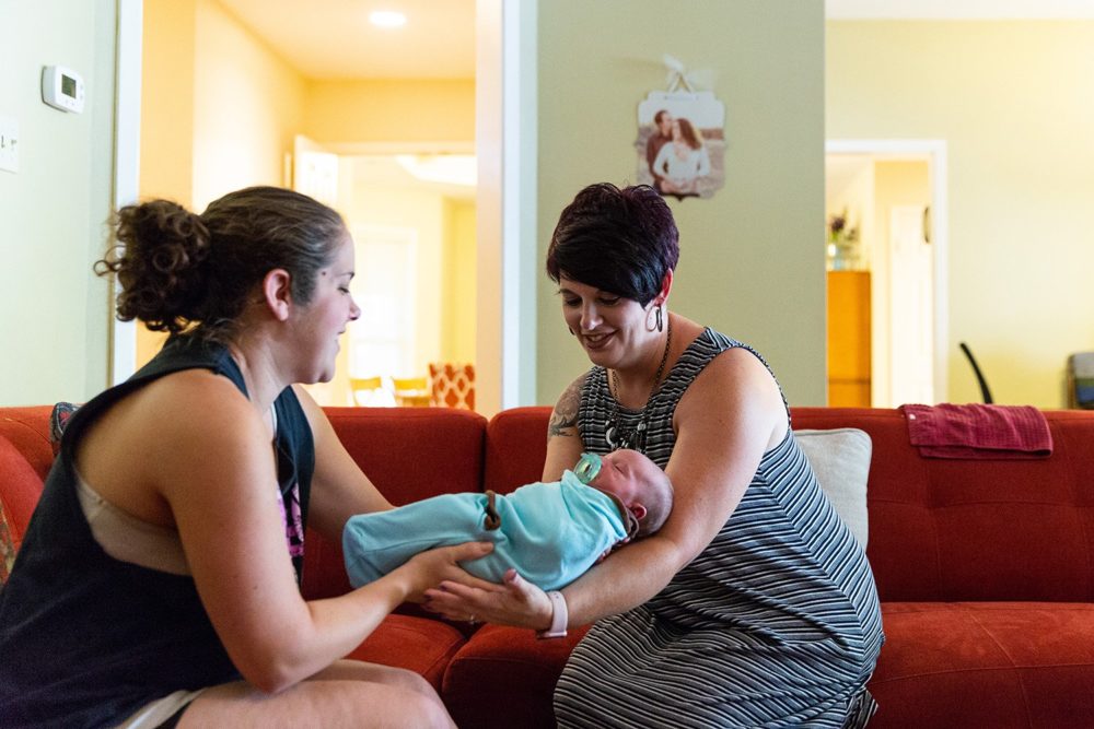 Hailey Frazier (left) gives her son Isaac to Sabrina Elliott (right), a doula in Abilene, during a home visit.  Gary Rhodes for The Texas Tribune
