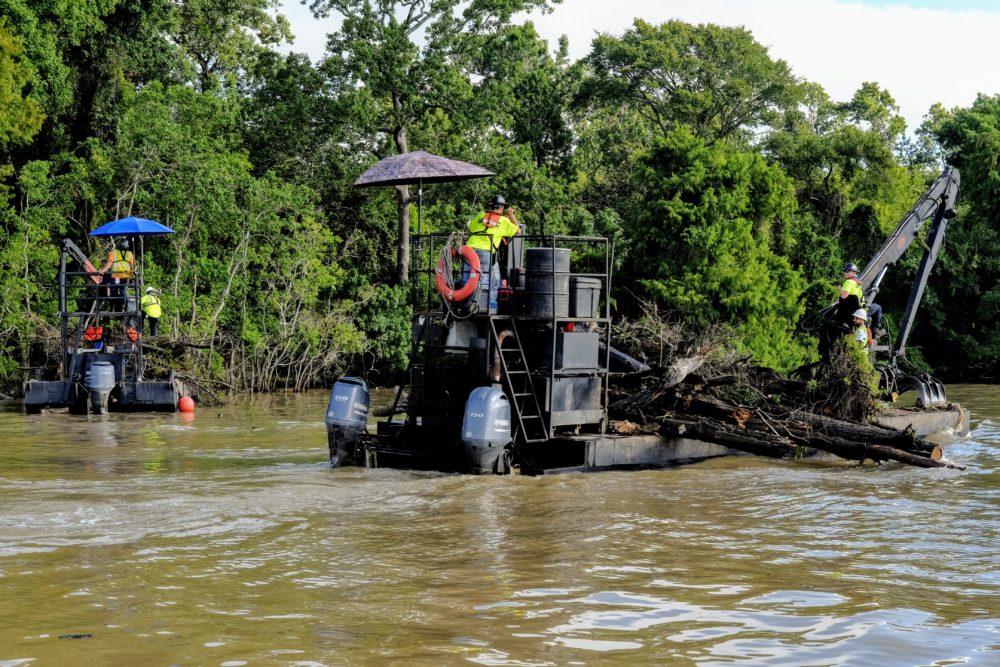 Workers on barges grab debris out of Lake Houston on July 5, 2018.