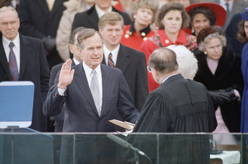 Pres. George H. W. Bush, left, raises his hand as he takes the oath of office as President of the United States outside the Capitol, Friday, Jan. 20, 1989, Washington, D.C. Vice Pres. Dan Quayle watches from behind.