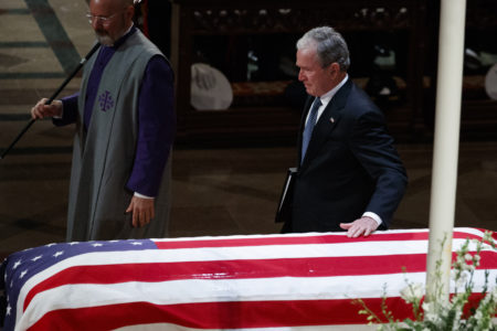 Former President George W. Bush touches his fathers casket after speaking during the State Funeral for former President George H.W. Bush, at the National Cathedral, Wednesday, Dec. 5, 2018, in Washington. (AP Photo/Evan Vucci)