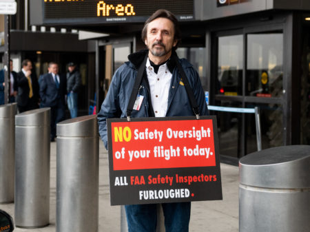 A man holds a placard at Newark Liberty International Airport on Tuesday, reminding travelers that FAA safety inspectors have been furloughed during the shutdown.