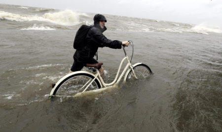 Tyler Holland guides his bike through the water as winds from Tropical Storm Barry push water from Lake Pontchartrain over the seawall Saturday, July 13, 2019, in Mandeville, La.