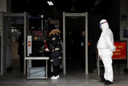 As the country is hit by an outbreak of the new coronavirus, a worker in protective suit looks on as a woman enters the Xizhimen subway station in Beijing, China on Jan. 27, 2020.
