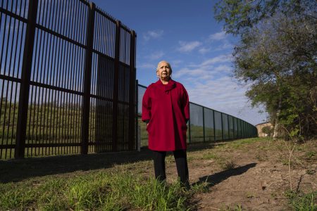 Juliet García, former president of the University of Texas at Brownsville, stands behind the border wall.