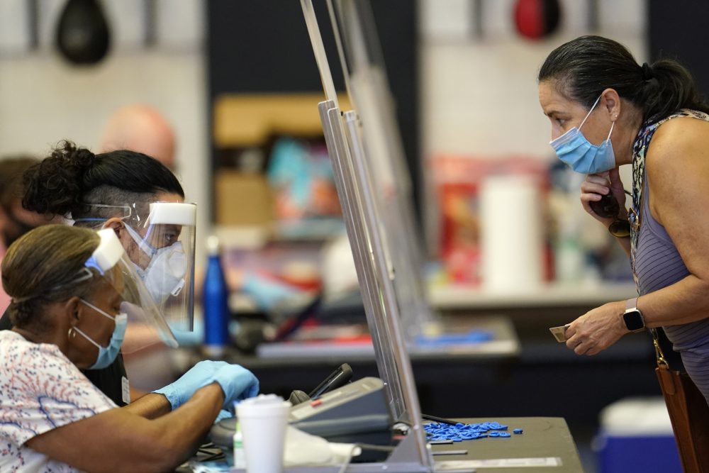 A voter, right, shows her identification to a Harris County election clerk before voting, Tuesday, July 14, 2020, in Houston.