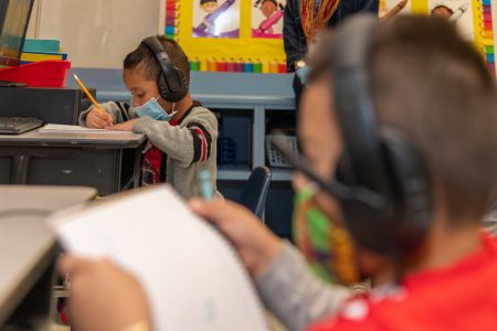 Two elementary-age boys study while wearing maskes and headphones.