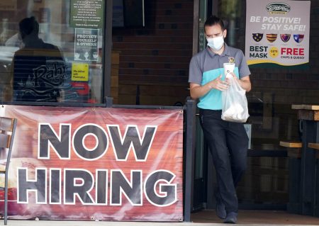 In this Sept. 2, 2020 file photo, a customer wears a face mask as they carry their order past a now hiring sign at an eatery in Richardson, Texas.