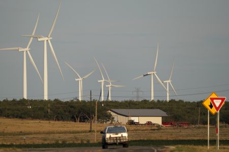 A vehicle makes its way down a rural road as wind turbines are shown at rear, Wednesday, July 29, 2020, near Sweetwater, Texas.