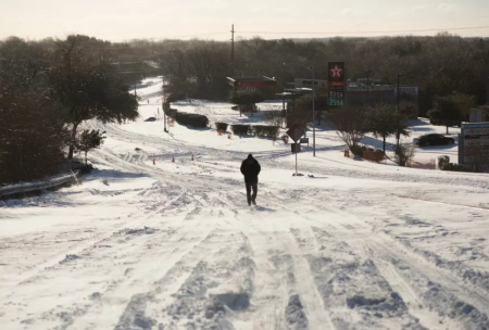 A pedestrian walks down an empty south Austin street Monday. Prolonged power outages have already upended Texans' lives as more wintry precipitation is expected across the state.