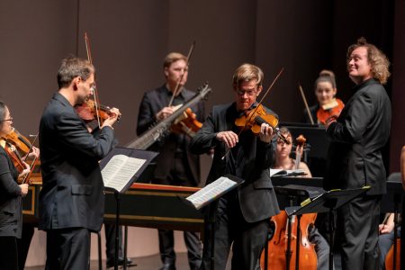 Photo of two violinists and orchestra
