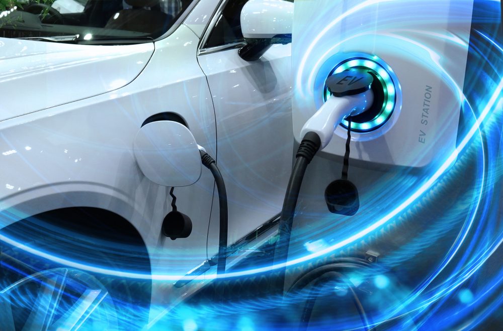 EV car or electric vehicle at charging station with power cable plugged in in blurred nature with blue energy effect. Environmentally friendly sustainable energy concept.