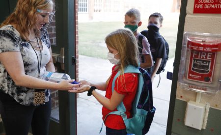 In this Aug. 5, 2020, file photo, wearing masks to prevent the spread of COVID19, elementary school students use hand sanitizer before entering school for classes in Godley, Texas. As schools reopen around the country, their ability to quickly identify and contain coronavirus outbreaks before they get out of hand is about to be put to the test.