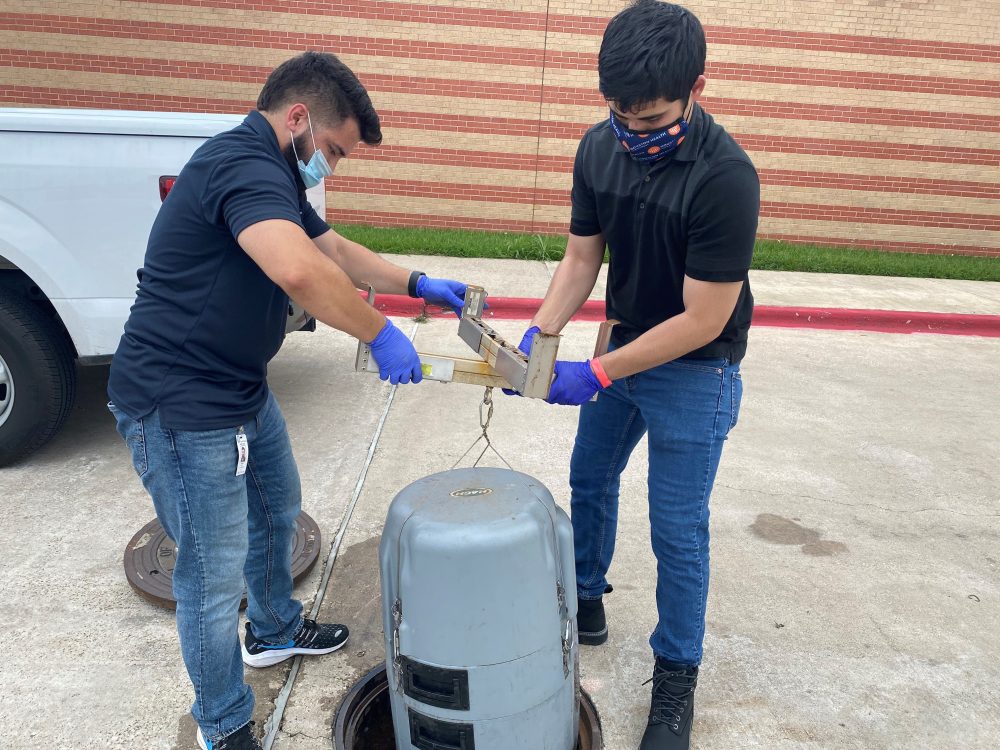 Houston health workers lift the sampling device back into the manhole where it collects sewage samples from an elementary school. 