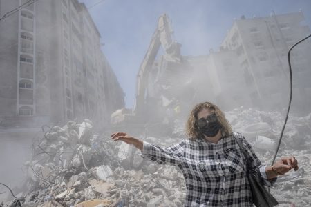 Pedestrians pass through clouds of dust as heavy construction equipment is used to sift through rubble to uncover valuables before it is transported away from the scene of a building destroyed in an airstrike prior to a cease-fire that halted an 11-day war between Gaza's Hamas rulers and Israel, Thursday, May 27, 2021, in Gaza City.