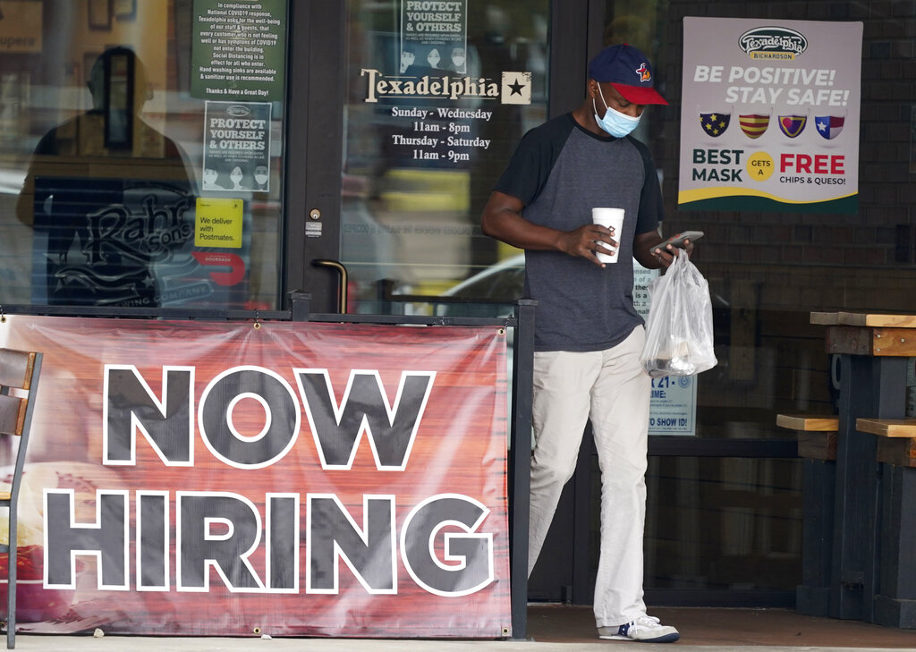 A customer wears a mask and looks at their cell phone as they carry their order past a now hiring sign at an eatery in Richardson, Texas, Wednesday, Sept. 2, 2020. The U.S. unemployment rate fell sharply in August to 8.4%  from 10.2% even as hiring slowed in August as employers added the fewest jobs since the pandemic began.