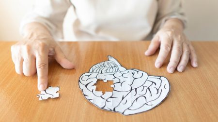 Elderly woman hands putting missing white jigsaw puzzle piece down into the place as a human brain shape. Creative idea for memory loss, dementia, Alzheimer's disease and mental health concept.