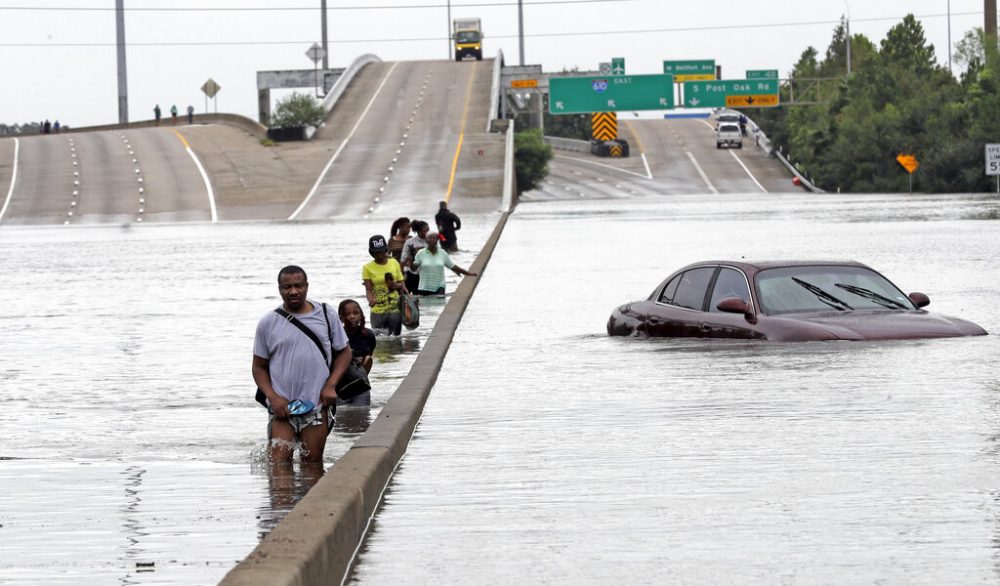 FILE - In this Aug. 27, 2017 file photo, evacuees wade through floodwaters from Tropical Storm Harvey on a section of Interstate 610 in Houston. Houston area officials expressed shock and anger on Friday, May 21, 2021, after learning that their communities, which suffered the brunt of damage from Hurricane Harvey, would be getting a fraction of $1 billion that Texas is awarding as part of an initial distribution of federal funding given to the state for flood mitigation.