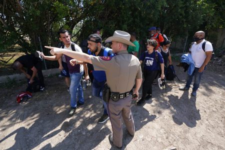 In this Wednesday, June 16, 2021 file photo, A Texas Department of Public Safety officer in Del Rio, Texas directs a group of migrants who crossed the border and turned themselves in. he Biden administration sued Texas on Friday, July 30, 2021 to prevent state troopers from stopping vehicles carrying migrants on grounds that they may spread COVID-19, warning that the practice would exacerbate problems amid high levels of crossings on the state's border with Mexico.