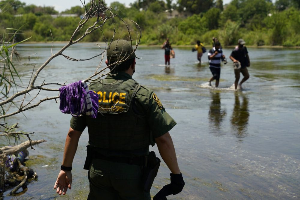 In this June 15, 2021, file photo, a Border Patrol agent watches as a group of migrants walk across the Rio Grande on their way to turning themselves in upon crossing the U.S.-Mexico border in Del Rio, Texas. A Justice Department attorney says the U.S. Centers for Disease Control and Prevention will issue an order this week about treatment of children under a public health order that has prevented migrants from seeking asylum at U.S. borders.