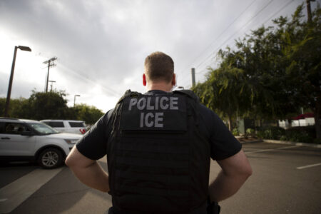 In this July 8, 2019, file photo, a U.S. Immigration and Customs Enforcement (ICE) officer looks on during an operation in Escondido, Calif. Advocacy groups and unions are pressuring Marriott, MGM and others not to house migrants who have been arrested by U.S. Immigration and Customs Enforcement agents. But the U.S. government says it sometimes needs bed space, and if hotels don’t help it might have to split up families.
