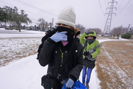 Amanda, left, and Rebecka try to keep warm as they walk to work during a light freezing rain in Dallas, Thursday, Feb. 3, 2022. A major winter storm with millions of Americans in its path is spreading rain, freezing rain and heavy snow further across the country.