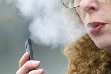 In this April 16, 2019 file photo, a woman exhales while vaping from a Juul pen e-cigarette in Vancouver, Wash. On Wednesday, Feb. 12, 2020, Massachusetts sued Juul Labs Inc., accusing the company of deliberating targeting young people through its marketing campaigns.