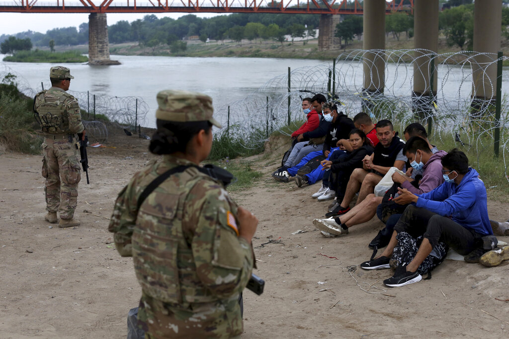 Migrants who had crossed the Rio Grande river into the U.S. are under custody of National Guard members as they await the arrival of U.S. Border Patrol agents in Eagle Pass, Texas, Friday, May 20, 2022. The Eagle Pass area has become increasingly a popular crossing corridor for migrants, especially those from outside Mexico and Central America, under Title 42 authority, which expels migrants without a chance to seek asylum on grounds of preventing the spread of COVID-19. A judge was expected to rule on a bid by Louisiana and 23 other states to keep Title 42 in effect before the Biden administration was to end it Monday.