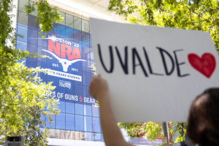 A protestor stands outside the annual NRA convention on My 27, 2022, holding a sign honoring the 19 kids and two adults killed in the Uvalde school shooting.