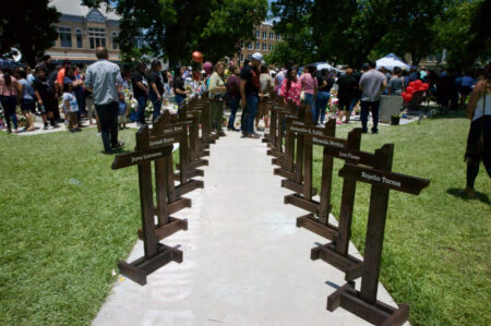 Wood crosses line a sidewalk leading to the makeshift memorial for the victims of the school shooting in Uvalde. People from all over the state have visited the small town to honor the victims of last week's deadly event.