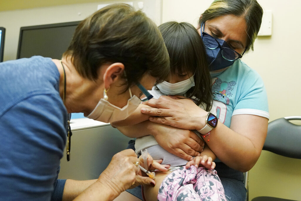 Deni Valenzuela, 2, center, is held by her mother, Xihuitl Mendoza, right, as she is given a Pfizer COVID-19 vaccine shot by nurse Deborah Sampson, left, Tuesday, June 21, 2022, at a University of Washington Medical Center clinic in Seattle. COVID-19 shots for children between six months and five years of age were given federal authorization over the weekend.