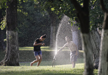 Youngsters cool off with water from grass sprinklers in a park in Bucharest, Romania, Wednesday, July 2, 2019.