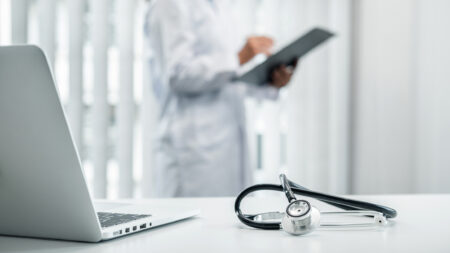 Doctor is standing and reading report and Stethoscope is on the table, doctor is reading symptoms of the patient and analyze treatment, health care and medicine at his hospital office